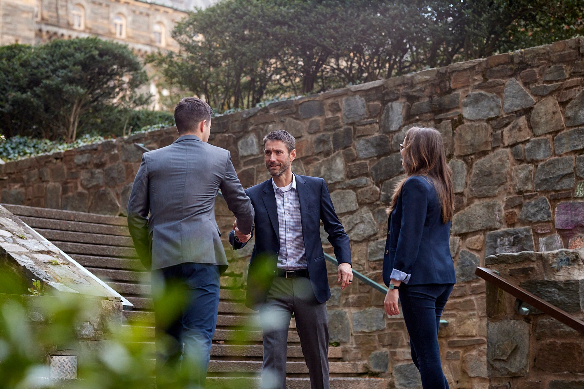 Matthew Cypher greeting two students in front of stone steps on the Georgetown campus.