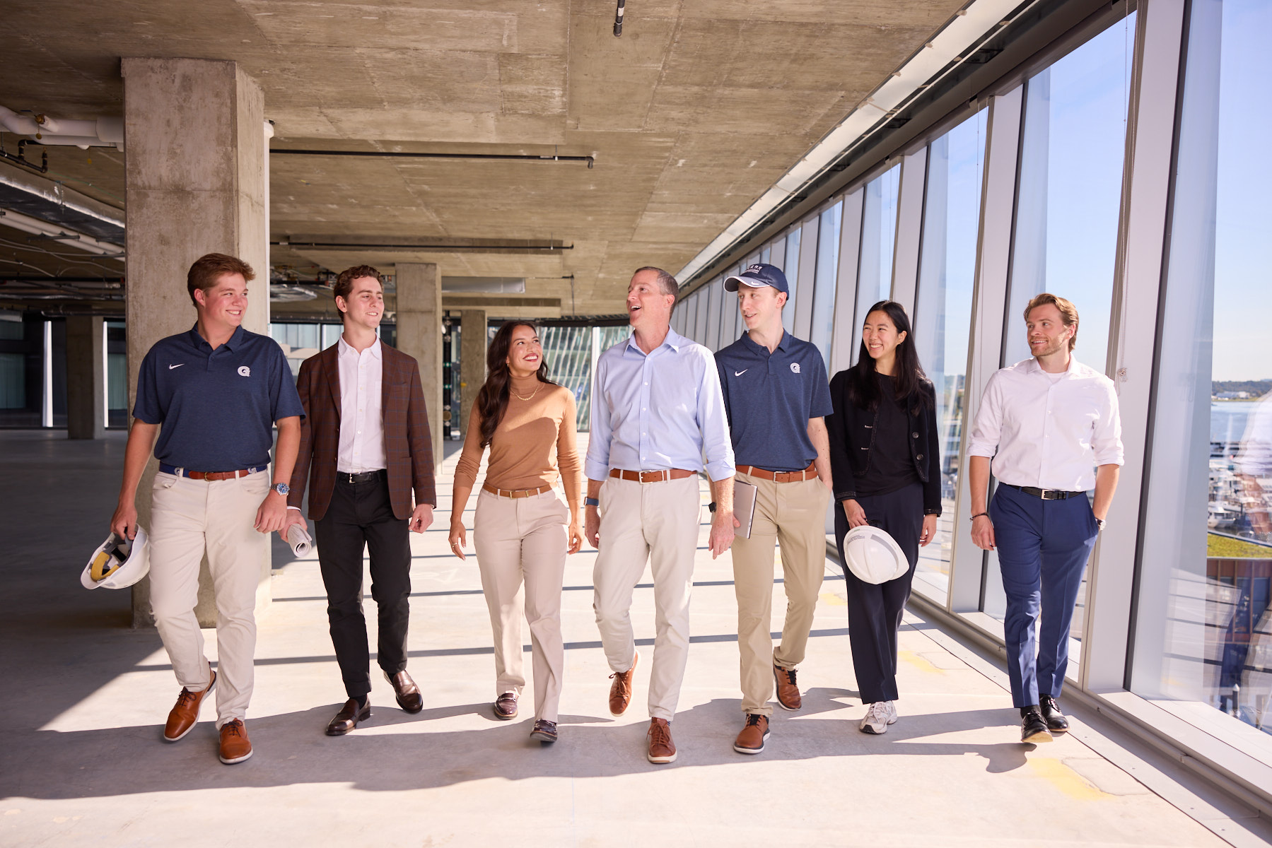 Exectuive Director, Tim Reardon (middle), walking with a group of Steers students during a site-tour walk through. Well-lit building hallway with large pane windows illuminating the space on a bight and clear sunny day.
