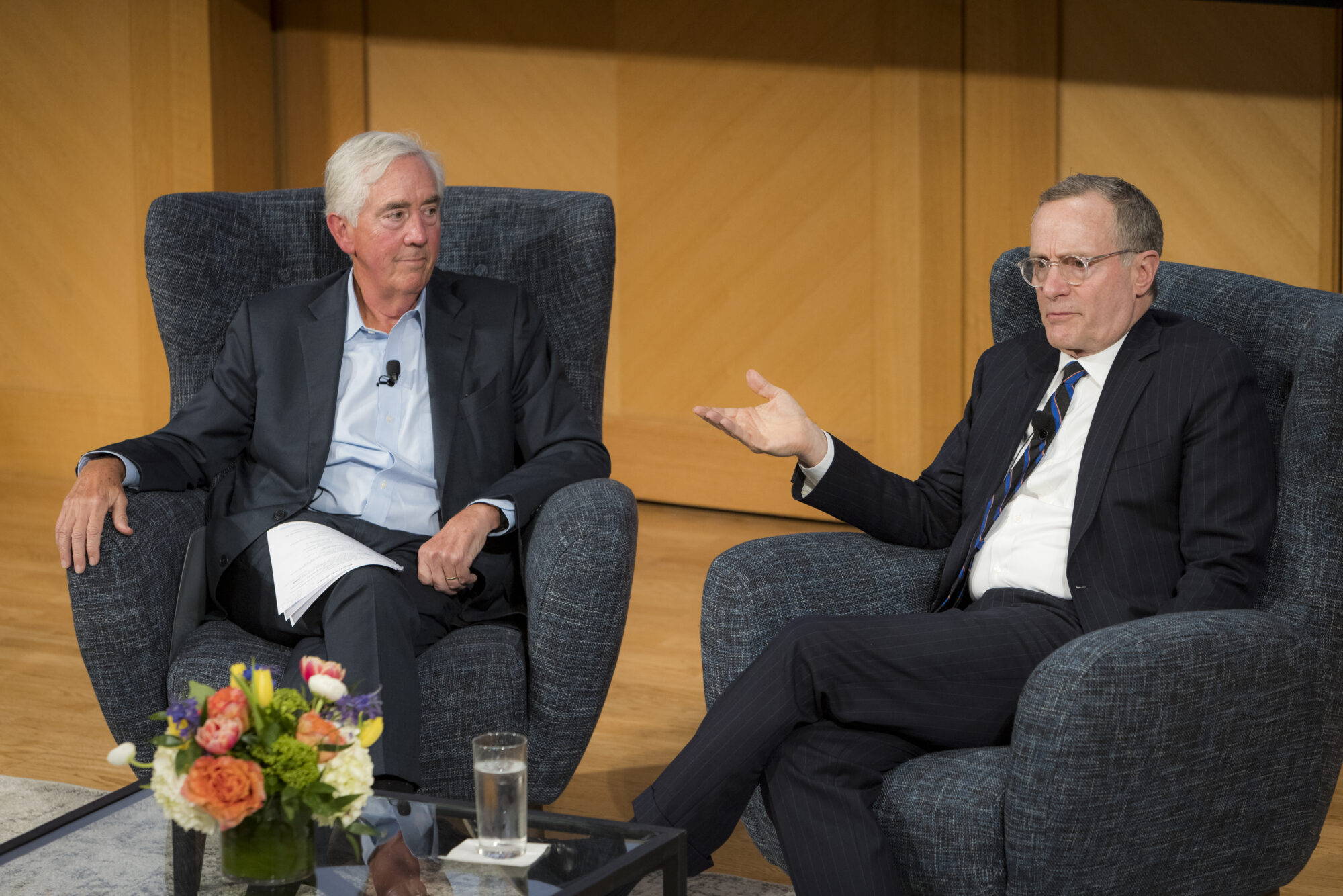 2023 Lumianries event with speaker, Howard Marks and moderator, Robert Steers, chatting in armchairs at the conference. Water bottles and floral decorations on top of a glass table in front of them. Well lit stage.